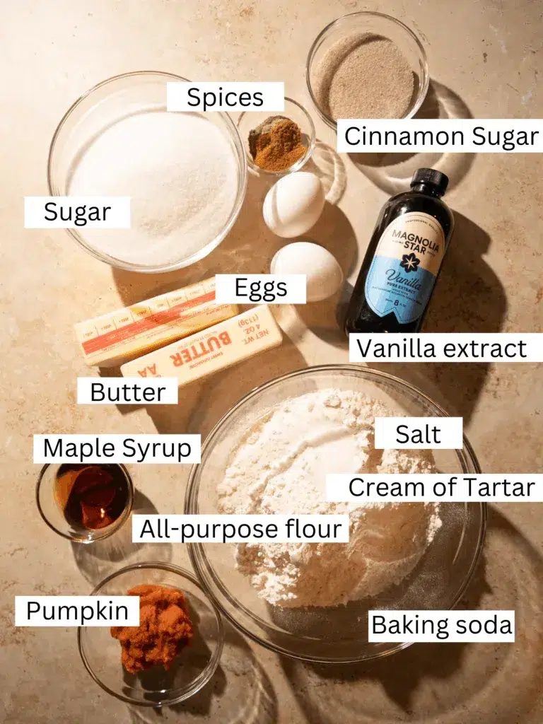 Overhead view of pumpkin chai snickerdoodle ingredients, including sugar, flour, pumpkin puree, maple syrup, butter, eggs, vanilla, spices, cream of tartar, baking soda, and cinnamon sugar.