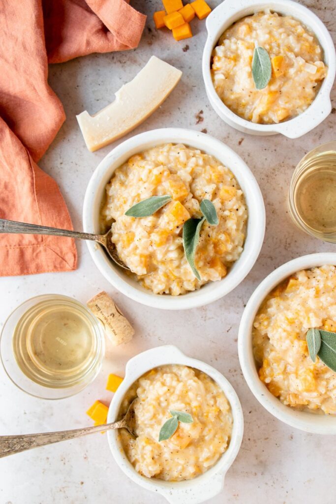 bowls of butternut squash risotto with glasses of wine and a block of parmesan 