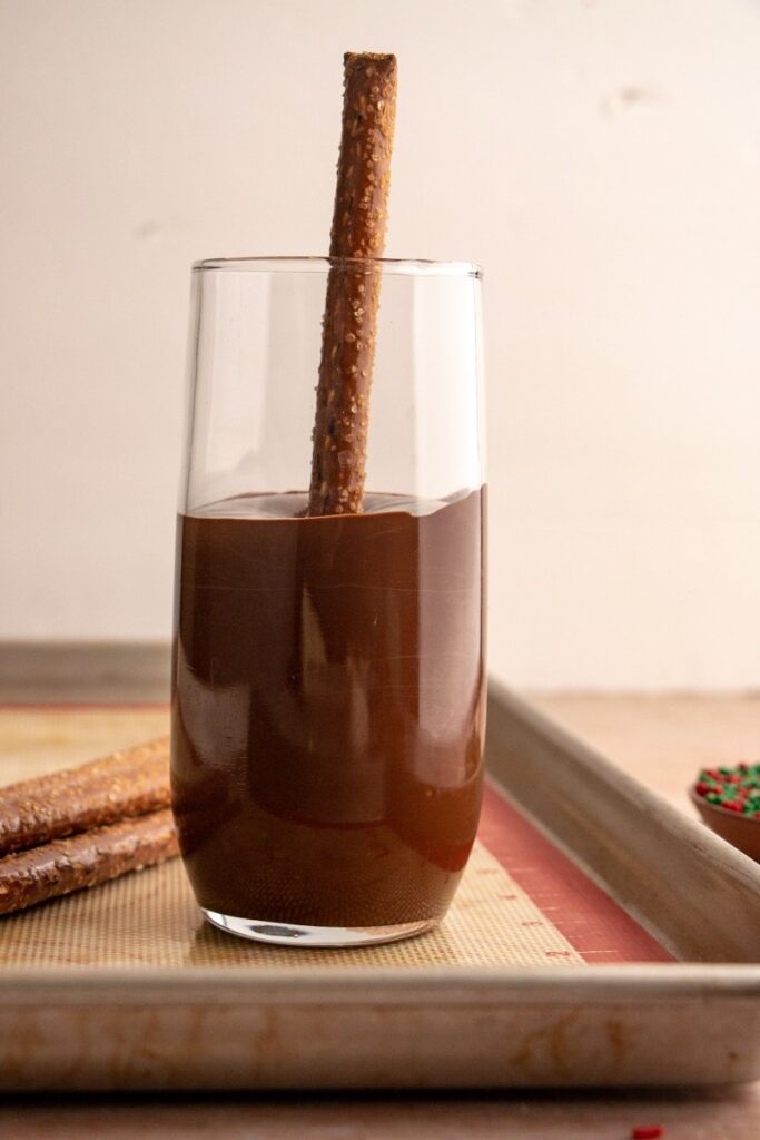 pretzel rod being dipped in a glass of chocolate 
