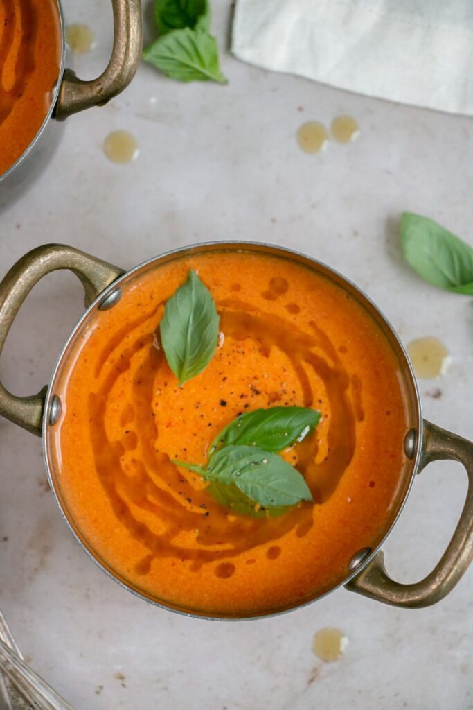 one bowl of red pepper tomato soup drizzled with basil oil