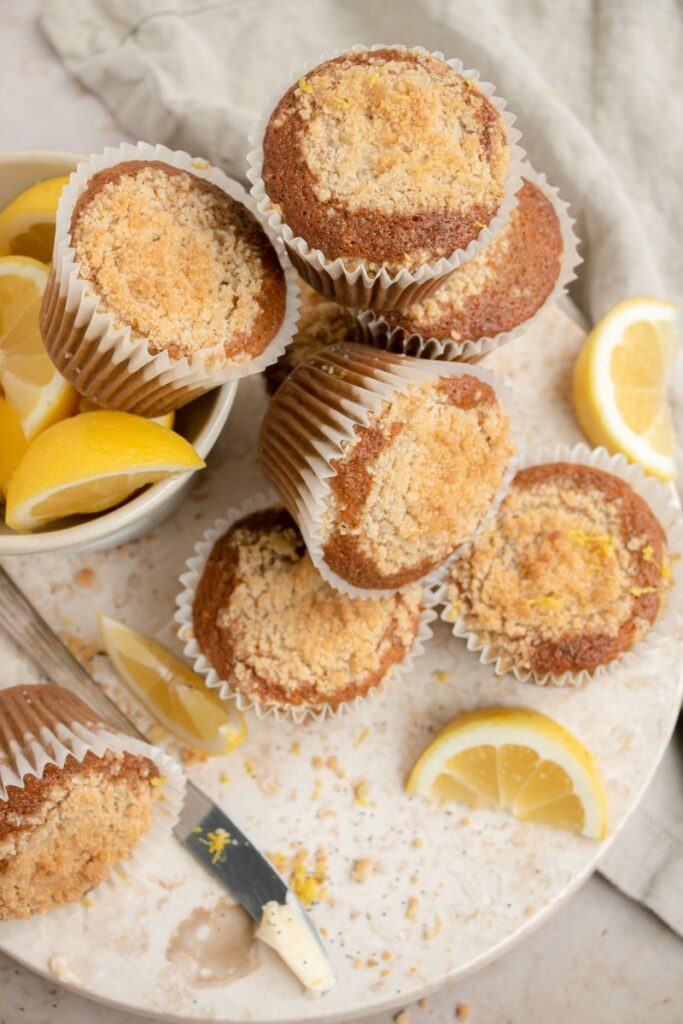 muffins scattered on a marble board with lemon wedges, crumbs, and a butter knife