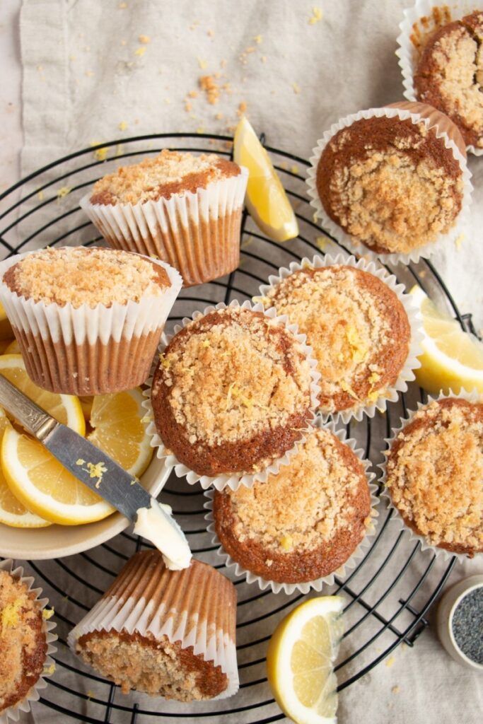 muffins scattered on cooling rack with a bowl of lemon wedges and butter on a knife