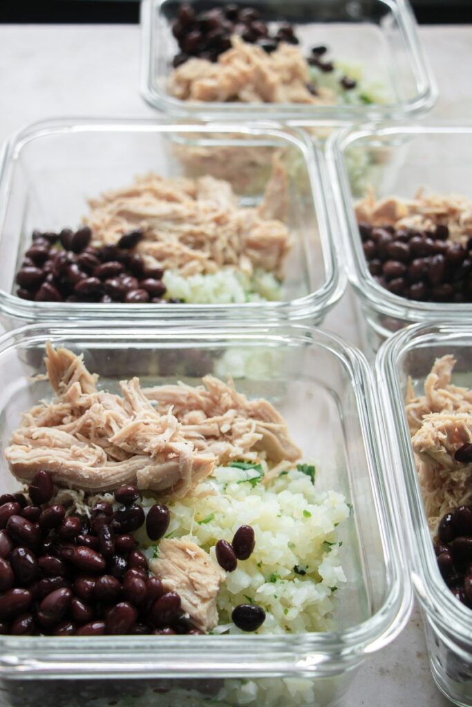 meal prep containers full of rice, beans, and shredded pork