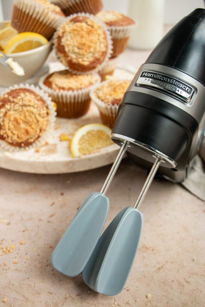 hamilton beach hand mixer with easy clean beaters and muffins in the back 