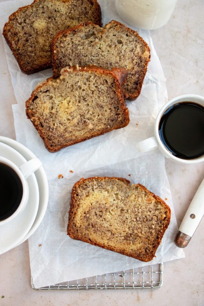 slices of banana bread on parchment paper with cups of espresso and a butter knife