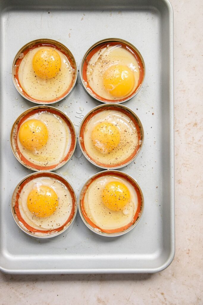 uncooked eggs in mason jar rings on a sheet pan