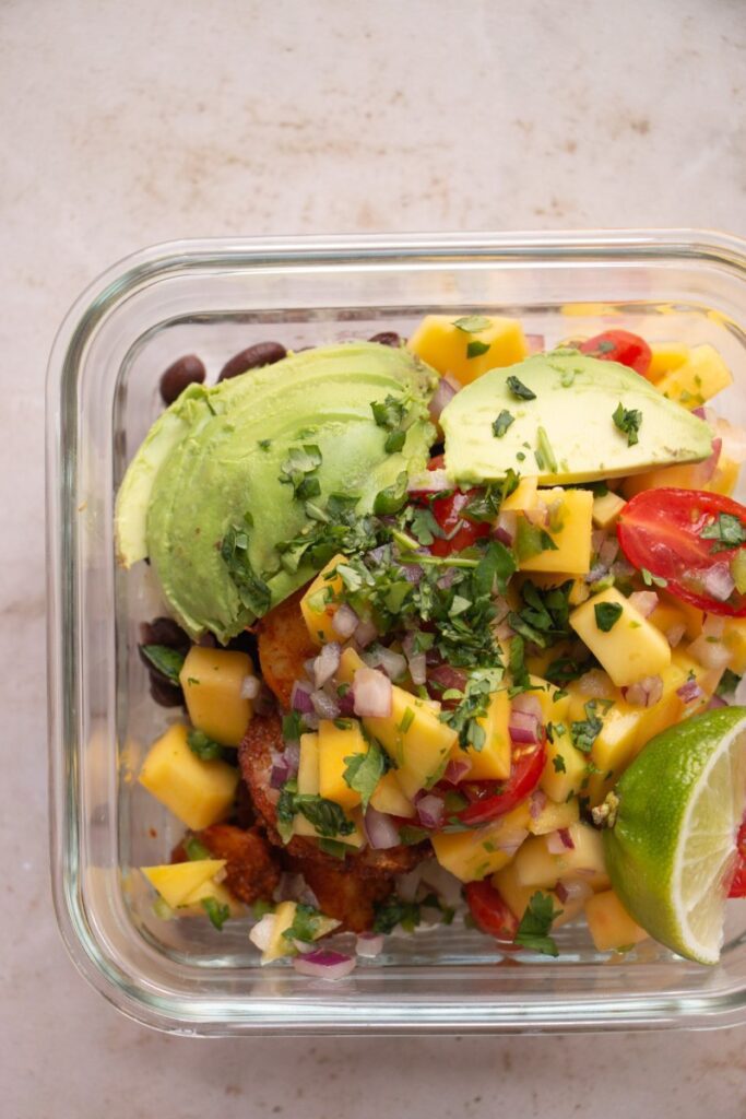 completed meal prep bowl topped with mango salsa, avocado, and fresh cilantro