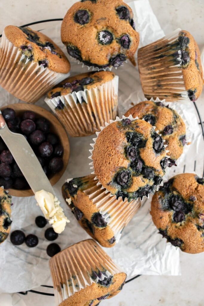 blueberry muffins on a cooling rack with a bowl of blueberries