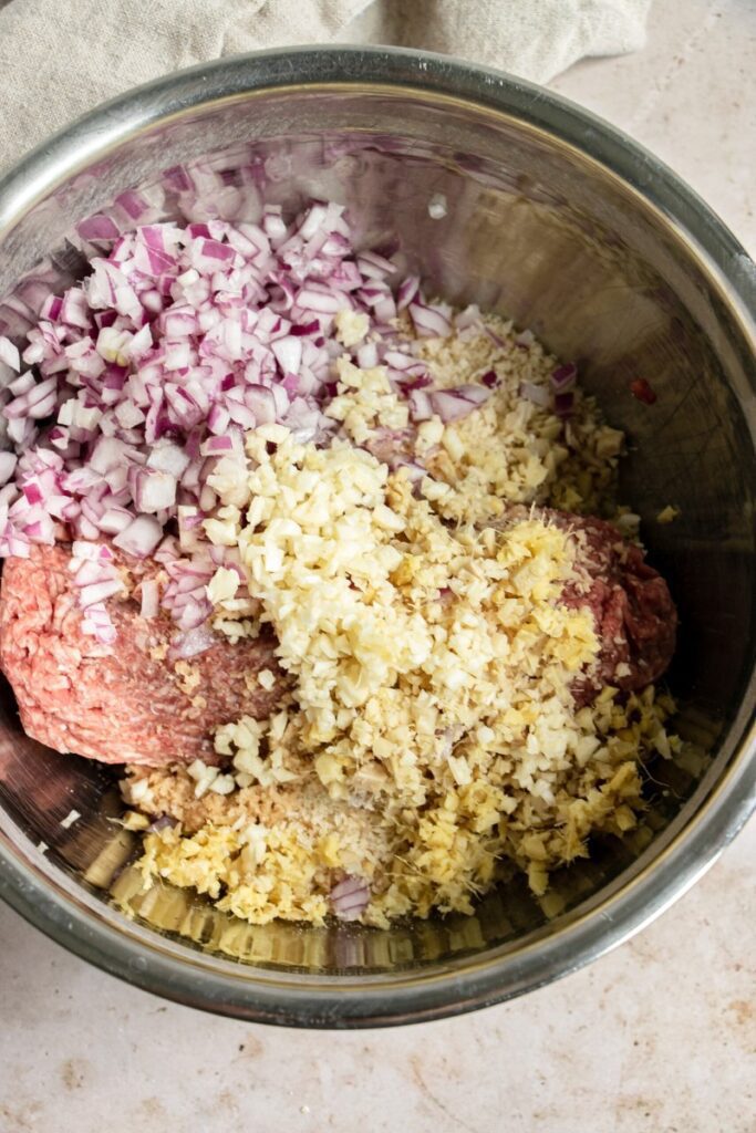 mixing bowl with ground beef, red onion, garlic, and ginger.