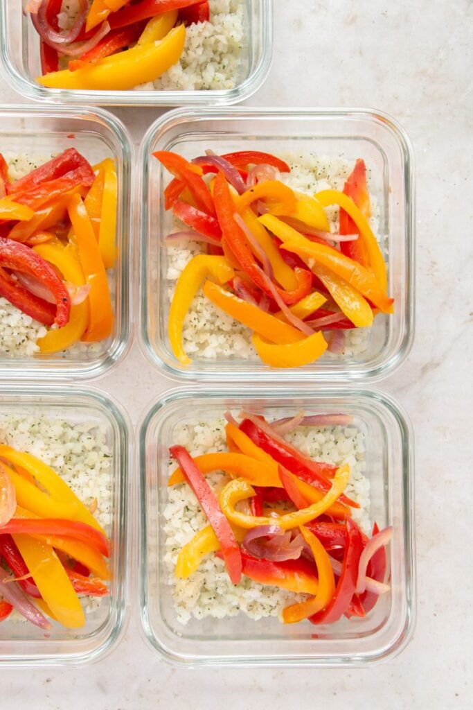 meal prep containers with cauliflower rice, peppers, and onions