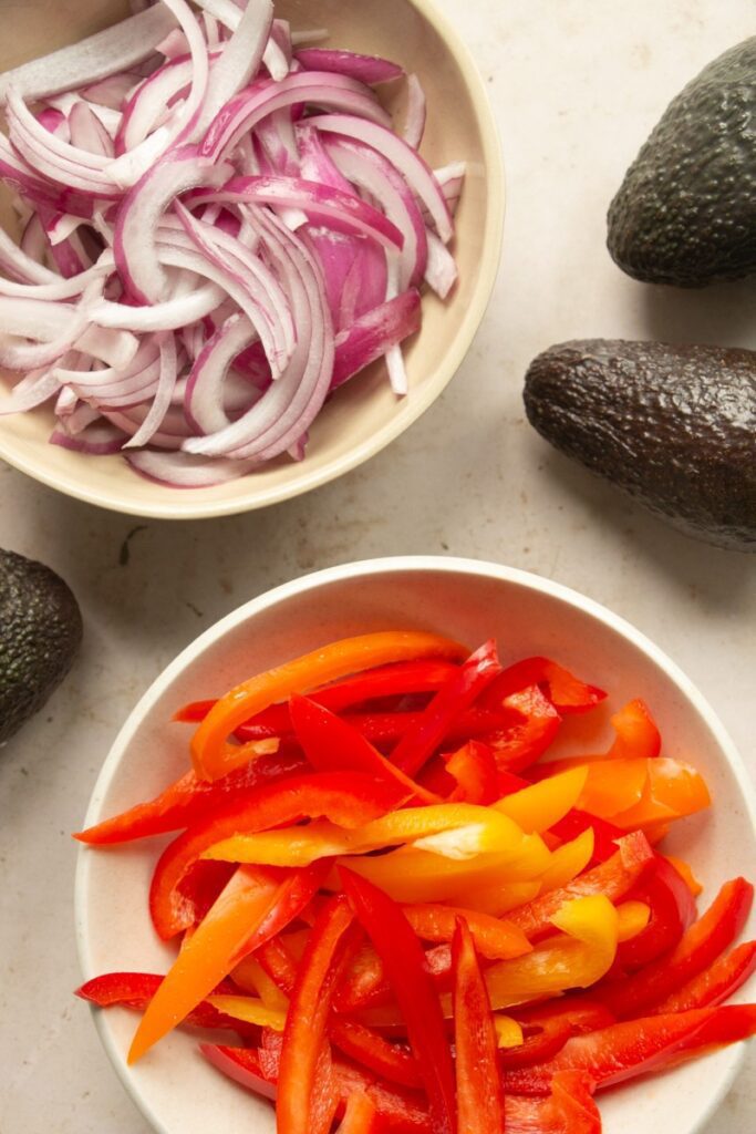 raw peppers and onions in bowls with avocados
