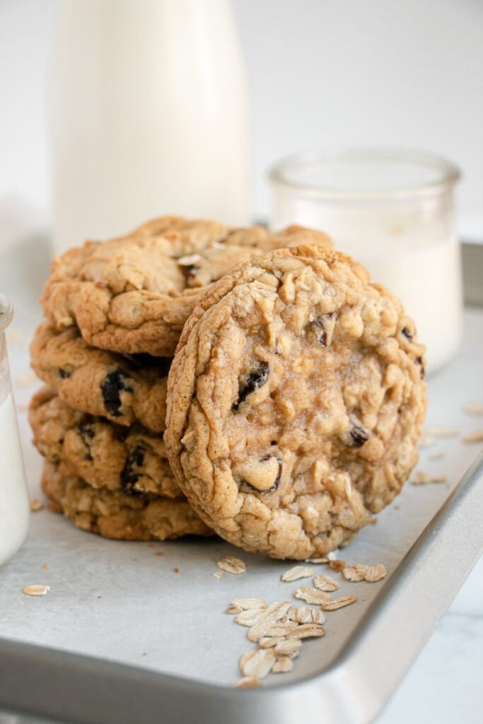 Easy Soft & Chewy Oatmeal Raisin Cookies stacked on a sheet tray with a glass of milk