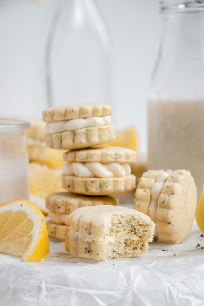 Lemon Poppy Seed Shortbread Sandwich Cookies with Lemon Buttercream stacked, one with a bite taken out.