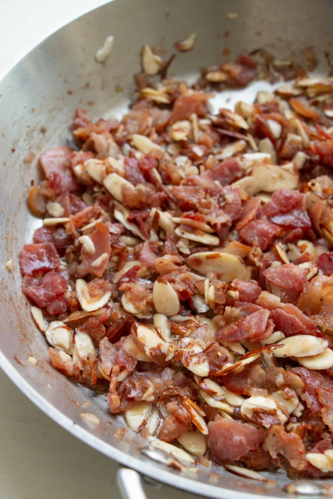 sauté pan with onion, garlic, bacon, an almonds 