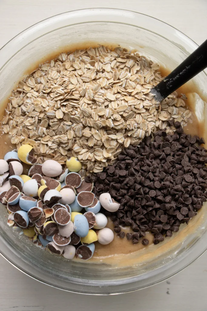 Cookie batter in a bowl with oats, chocolate chips, and mini eggs