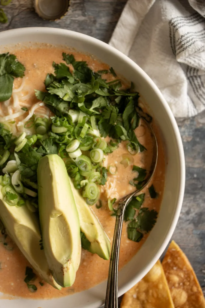 bowl of soup topped with avocado, cilantro, green onion, and shredded cheese