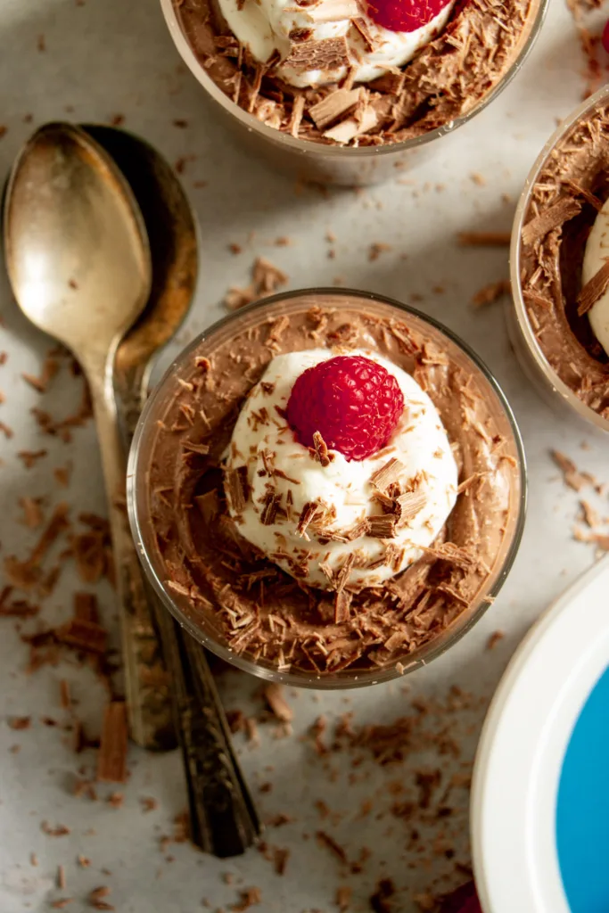 chocolate pudding topped with whipped cream, raspberries, and chocolate shavings