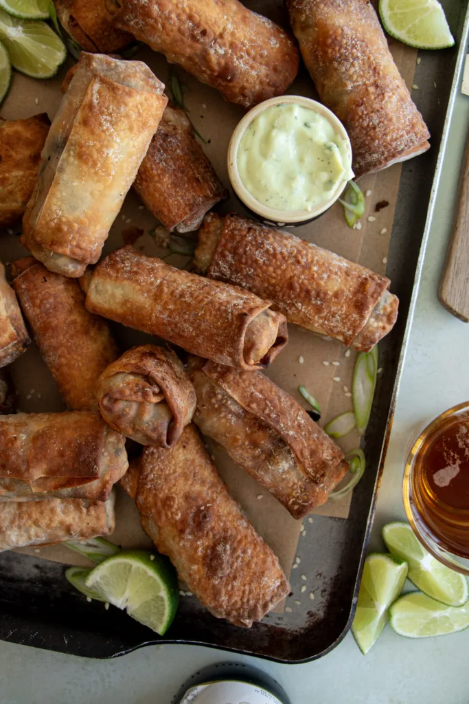 golden brown egg rolls on a serving tray with sauces 