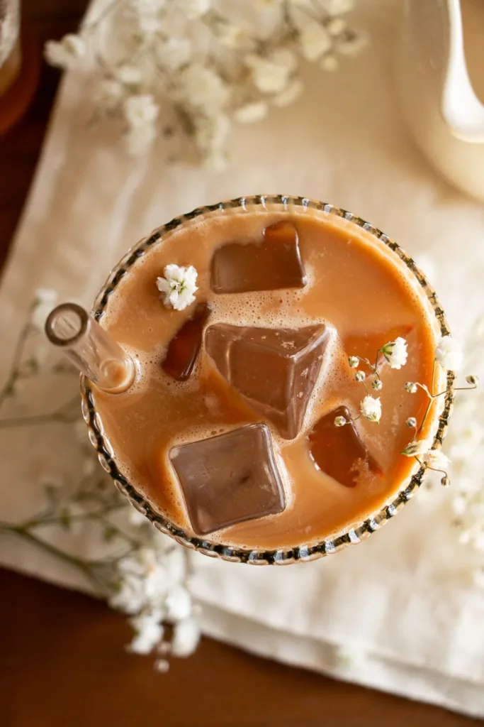glass of shaken espresso with oat milk ad small white flowers 