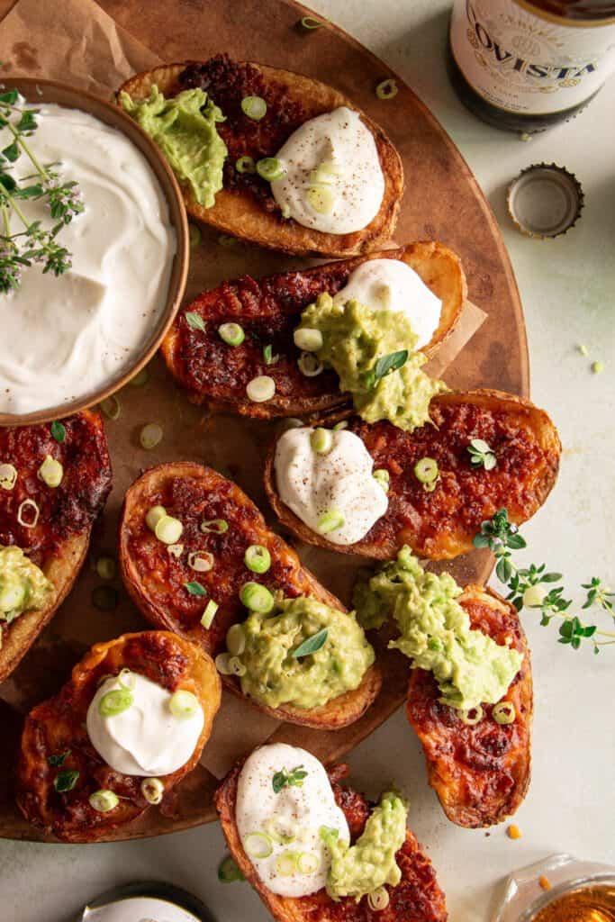 potato skins scattered on a tray with guacamole and sour cream and bottles of beer