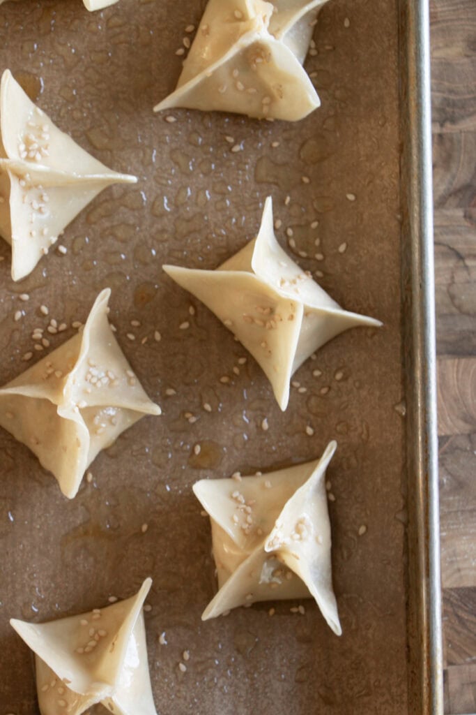 unbaked rangoons on a sheet pan with sesame seeds