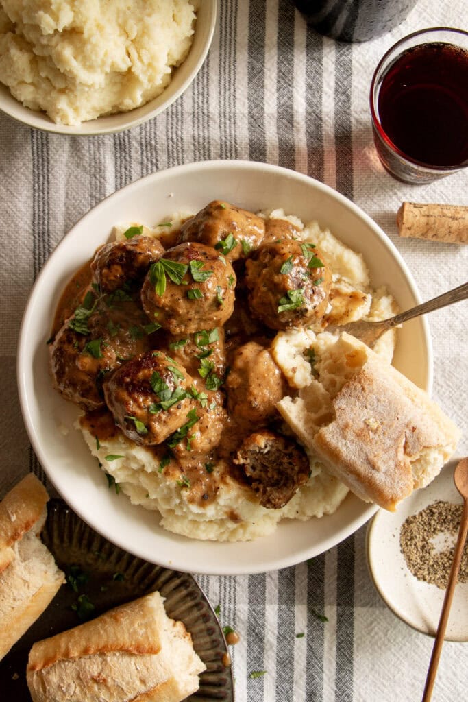 a big bowl of mashed potatoes topped with fresh meatballs and extra pan gravy with a baguette