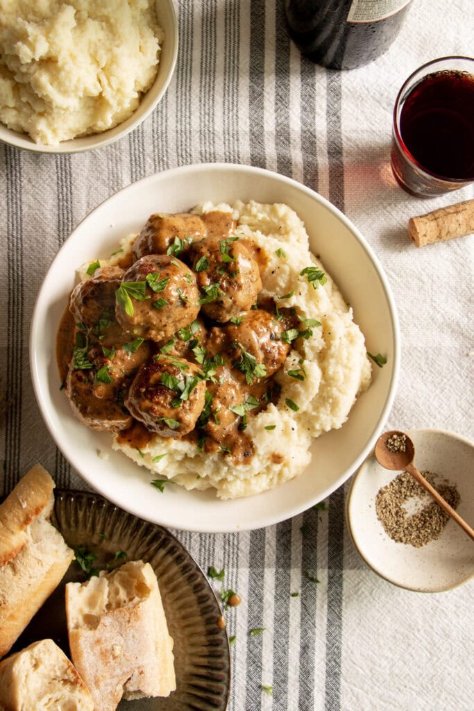 a table set with a bowl of mashed potatoes topped with Swedish meatballs 