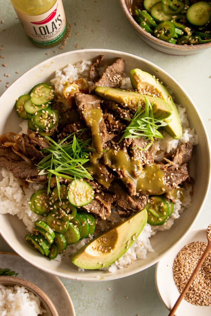 bowl of rice with sliced beef, cucumber salad, and cucumbers.