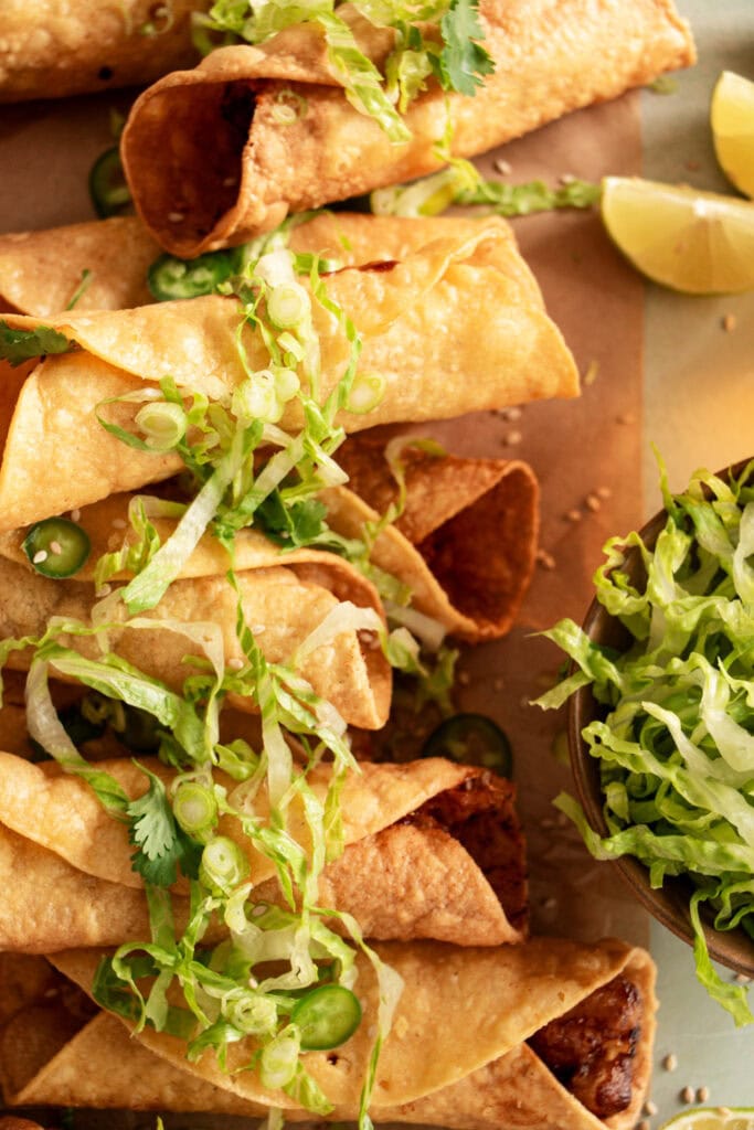 layered chicken taquitos on parchment topped with lettuce and jalapenos 