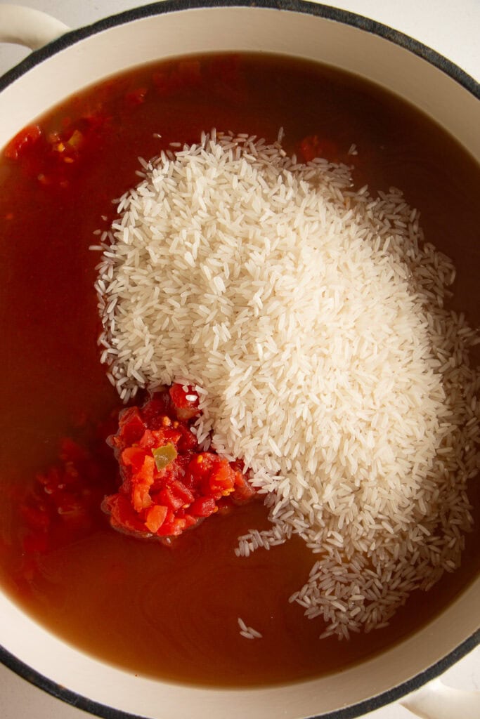 Skillet with uncooked rice, stock, diced tomatoes, and enchilada sauce. 