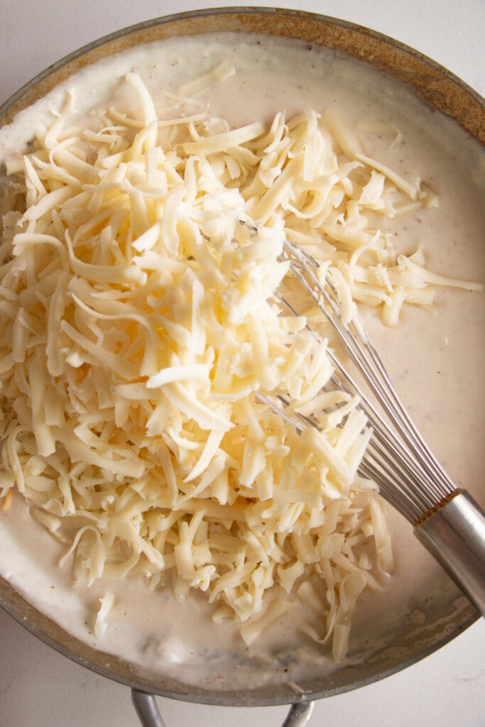 Shredded cheese in saucepan mixing into milk mixture
