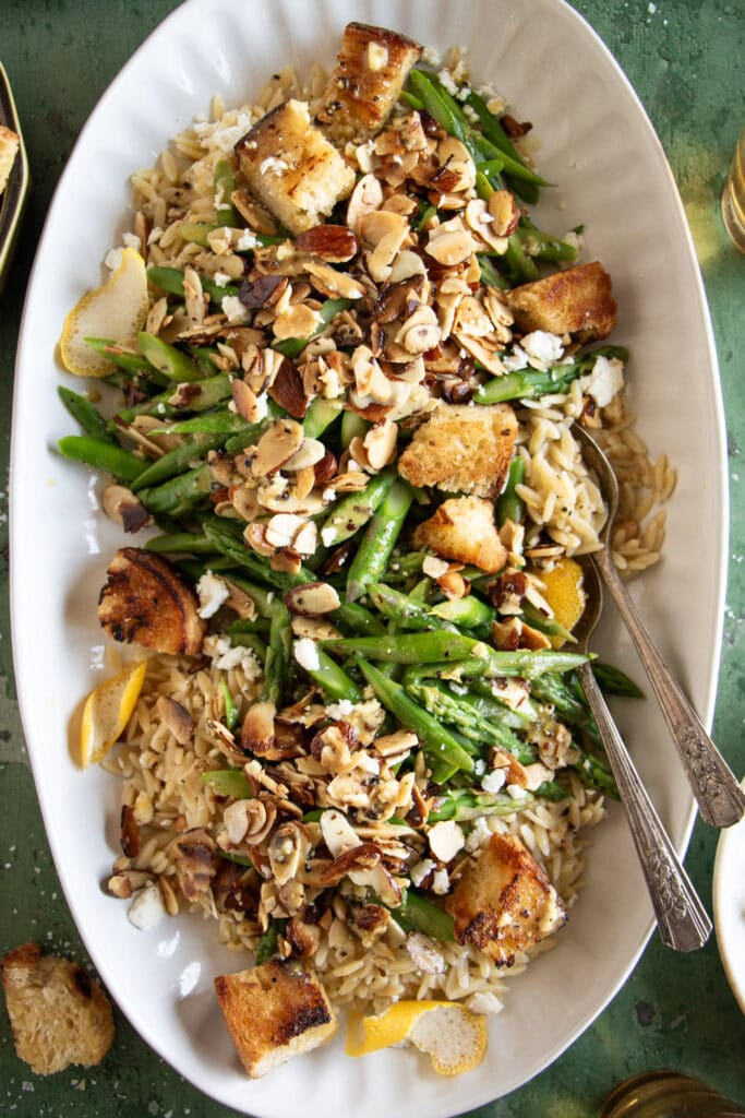 large platter with cold asparagus salad and serving spoons