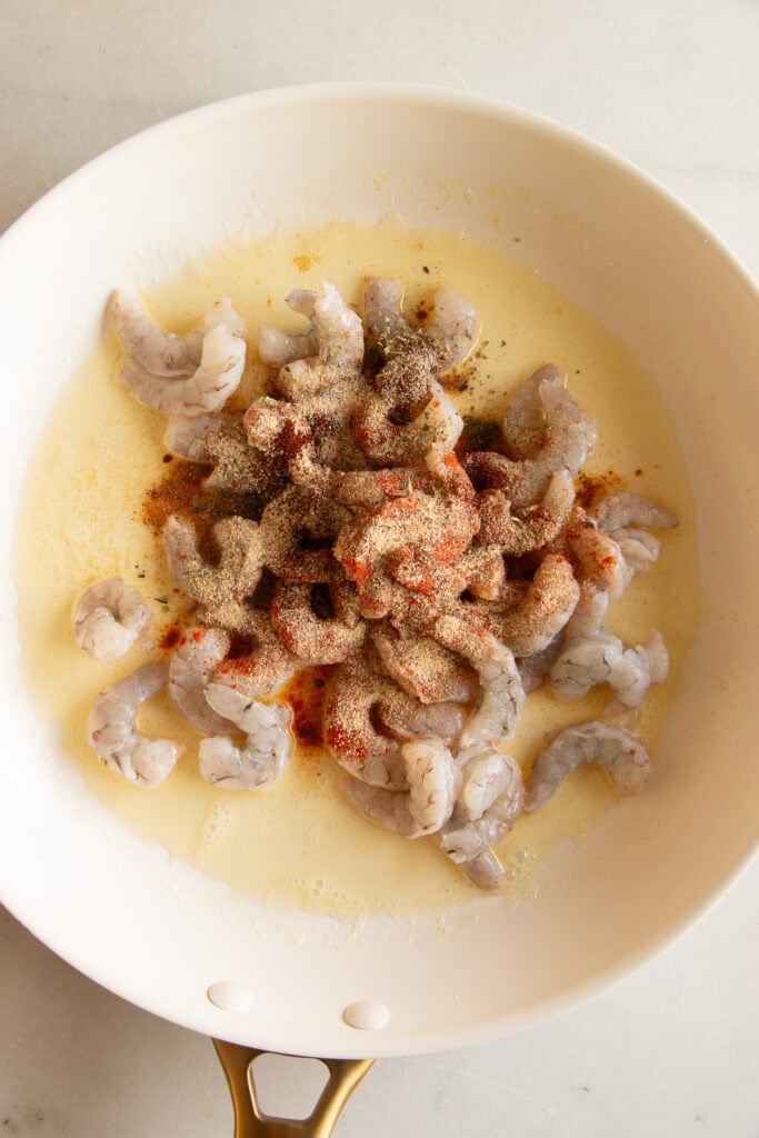 Sauté pan with melted butter, raw shrimp, and Cajun seasoning 