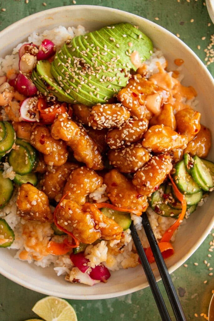 Rice bowl topped with honey chicken, sliced avocado, pickled veggies, and aioli. 
