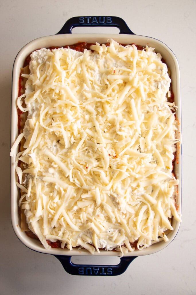 Layered lasagna in a casserole dish topped with shredded cheese