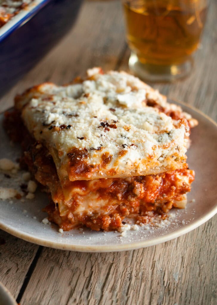 Small plate with a slice of layered lasagna sprinkled with extra parmesan cheese and red pepper flakes