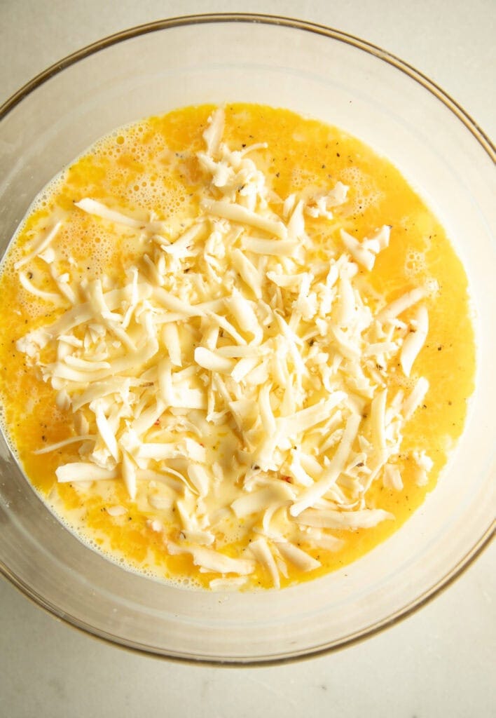 Mixing bowl with egg mixture and shredded cheese