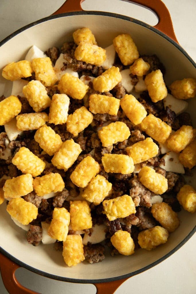 Chopped biscuit dough topped with crumbled sausage and tater tots in a casserole dish