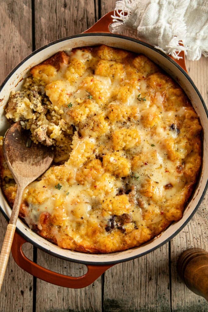 Large round casserole dish loaded with fresh baked egg casserole with a scoop taken out.
