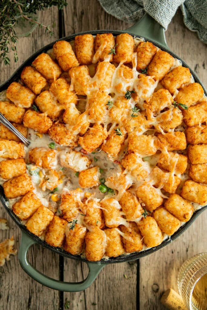 cast iron skillet with golden brown tater tot casserole topped with fresh thyme.
