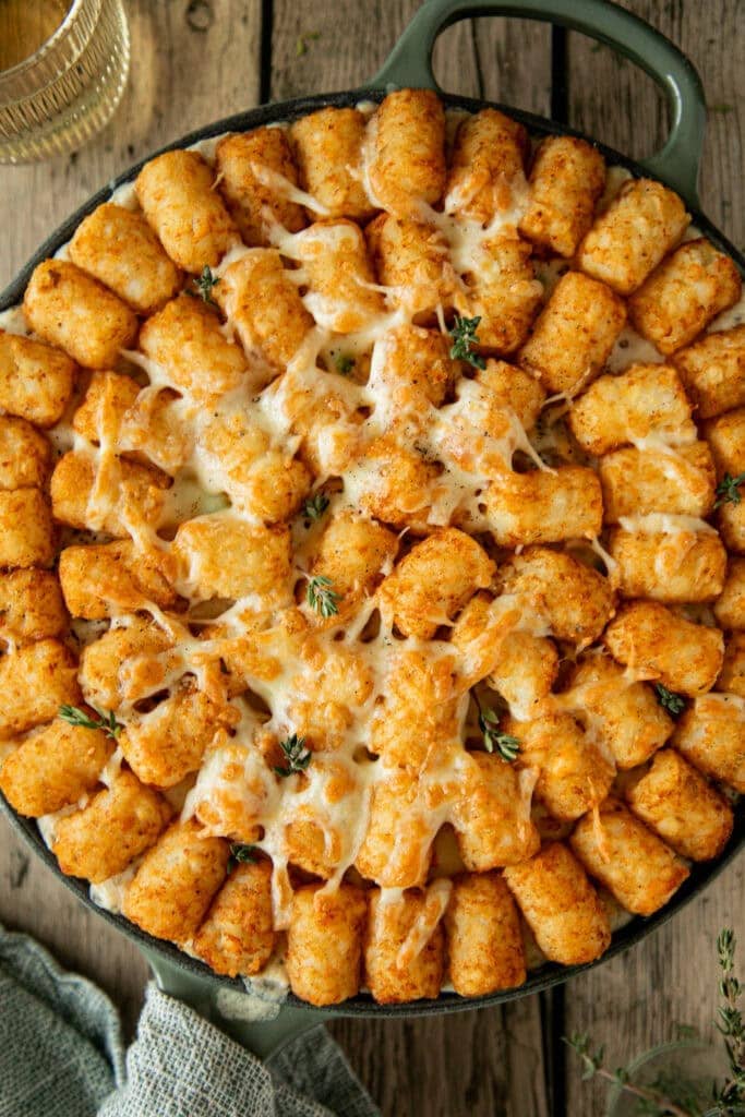 Cast iron skillet filled with tater tot casserole, topped with golden brown tater tots.