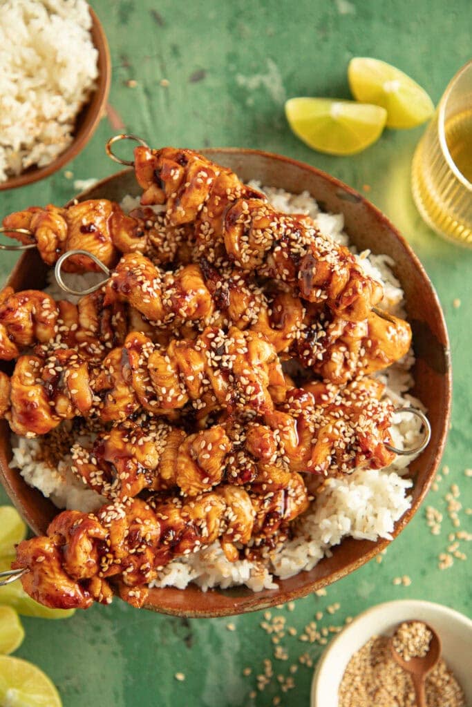 Bowl of white rice topped with chicken skewers and sesame seeds