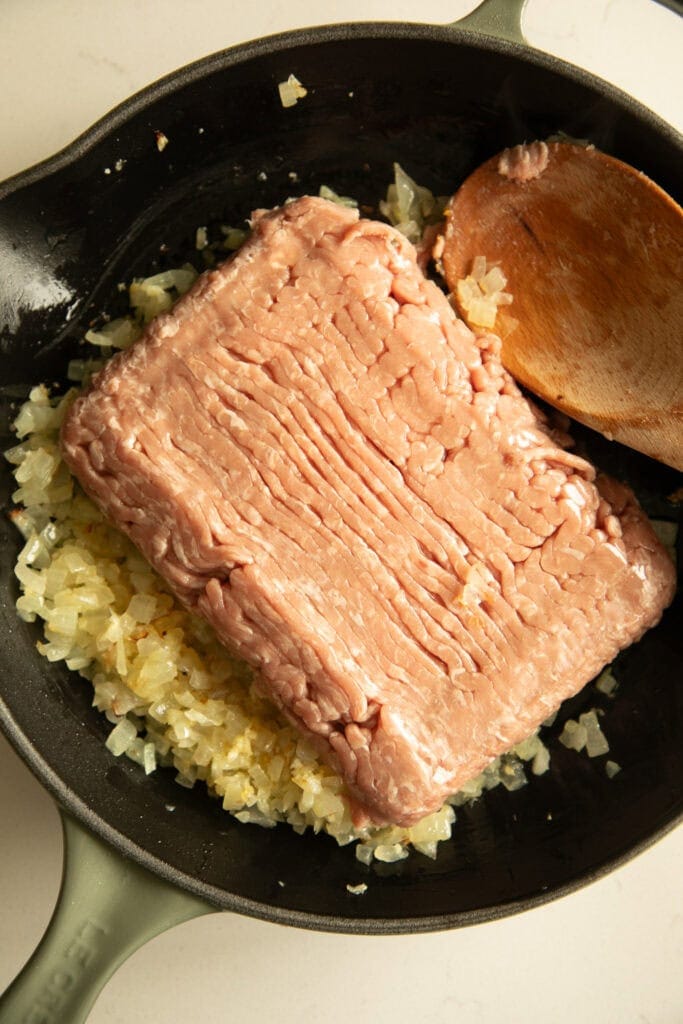 raw turkey going into sauteed onions and garlic