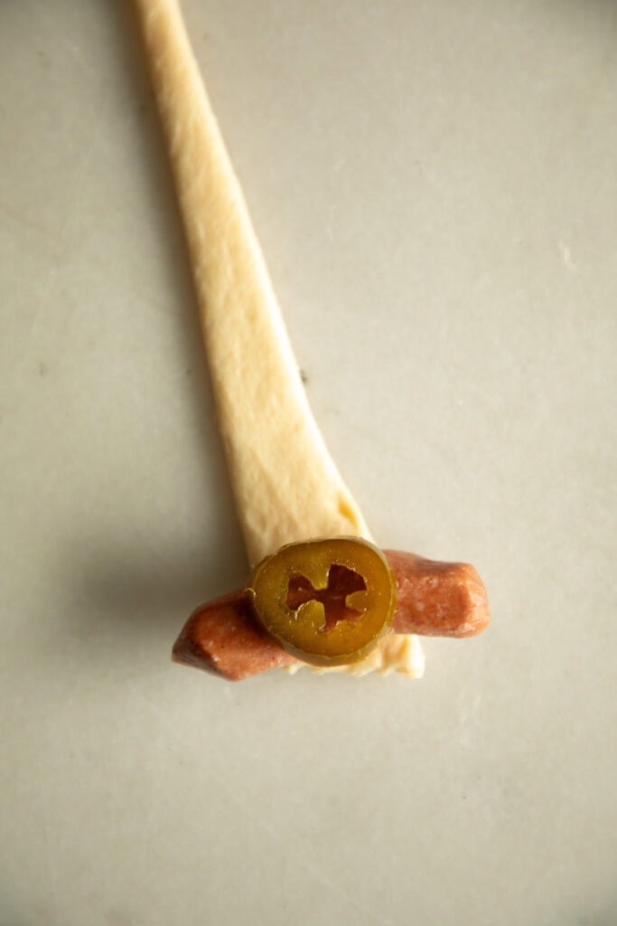 cocktail smokie on a piece of crescent roll dough with a sliced jalapeno