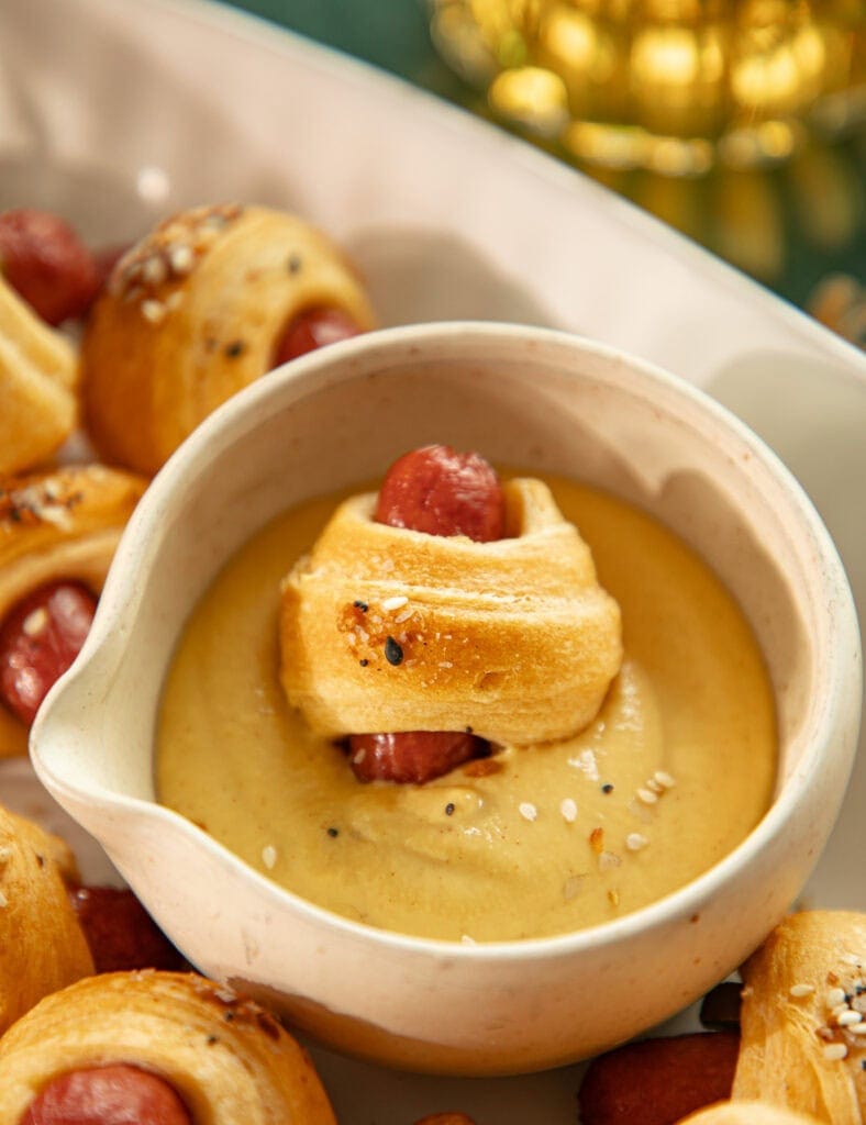 little smokie wrapped in dough being dipped in mustard