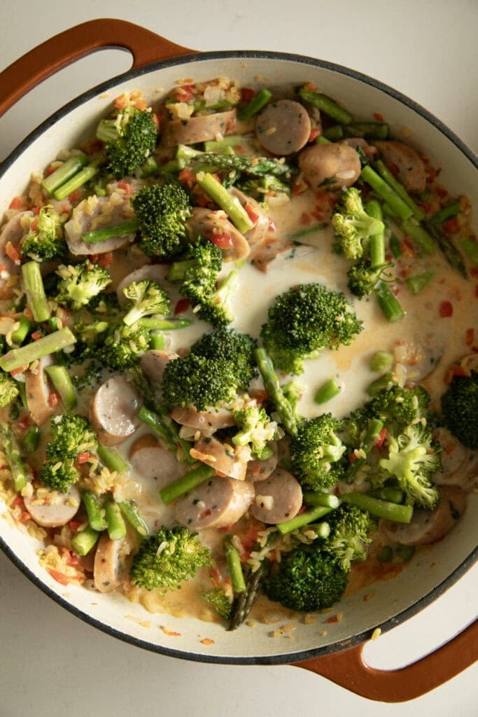Large pan with cooked veggies, sausage, and orzo covered in milk