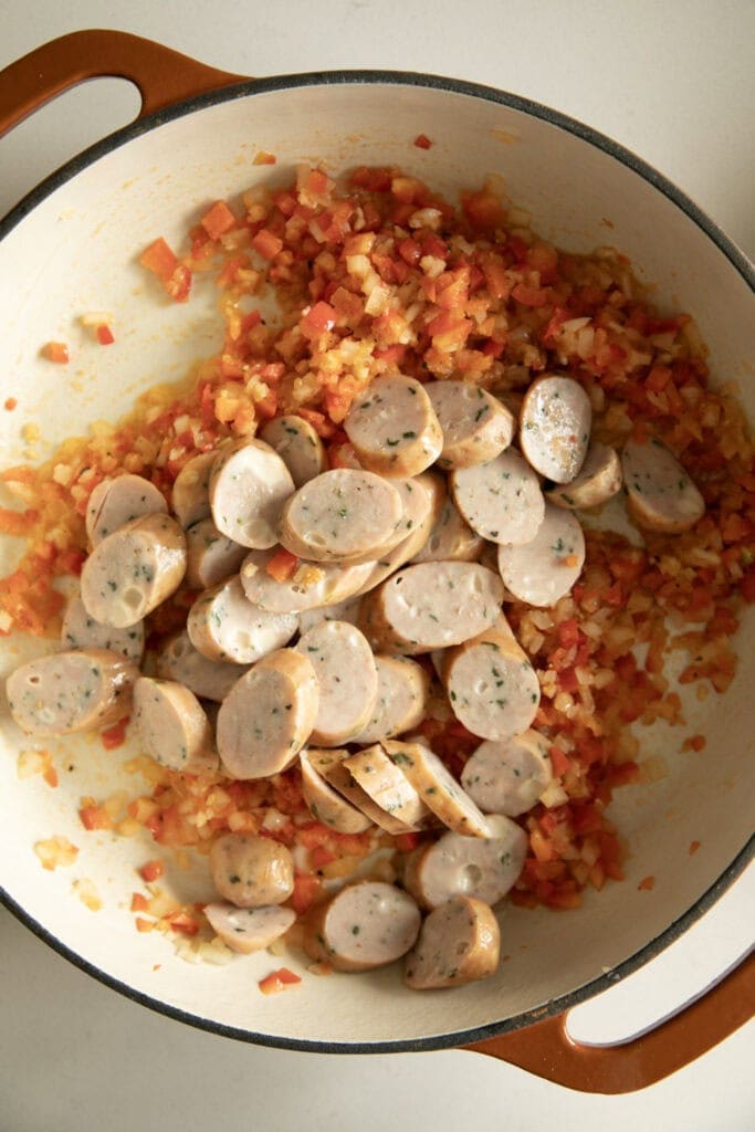 Sauteed vegetables in a large pan with sliced chicken sausage
