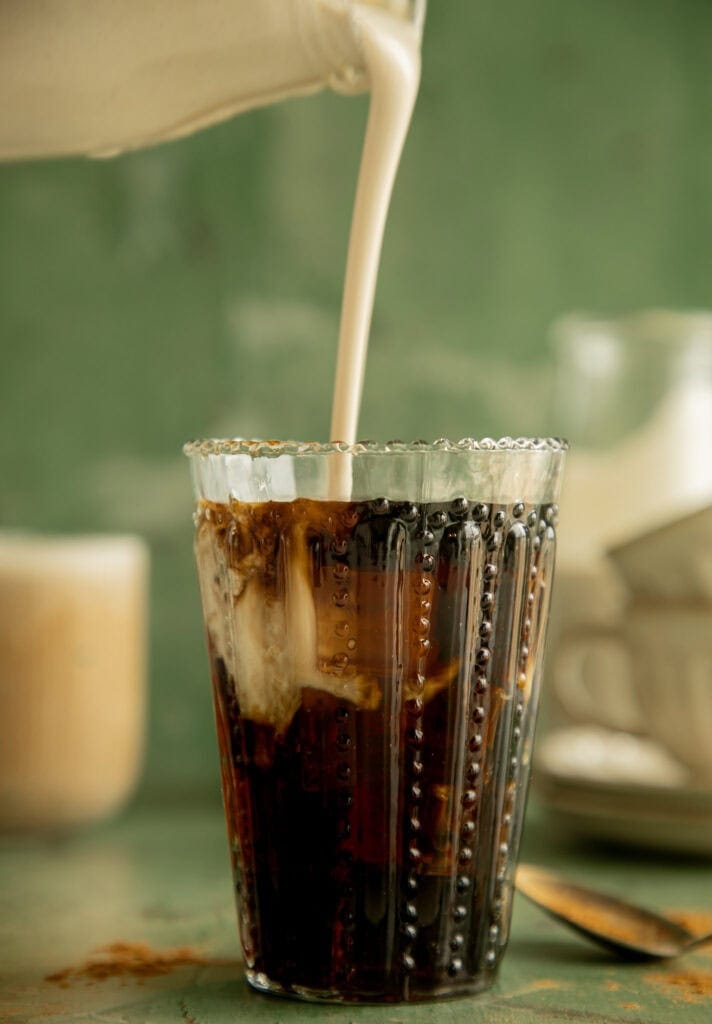 Glass of black iced coffee with a pour of cashew creamer
