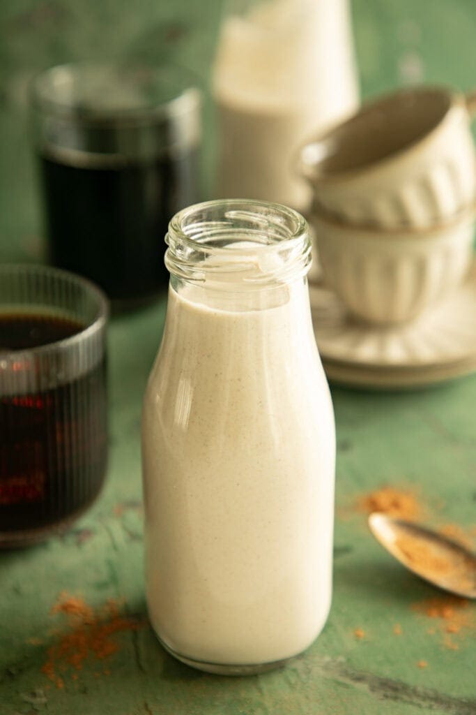 Glass bottle full of cashew creamer with glasses of coffee