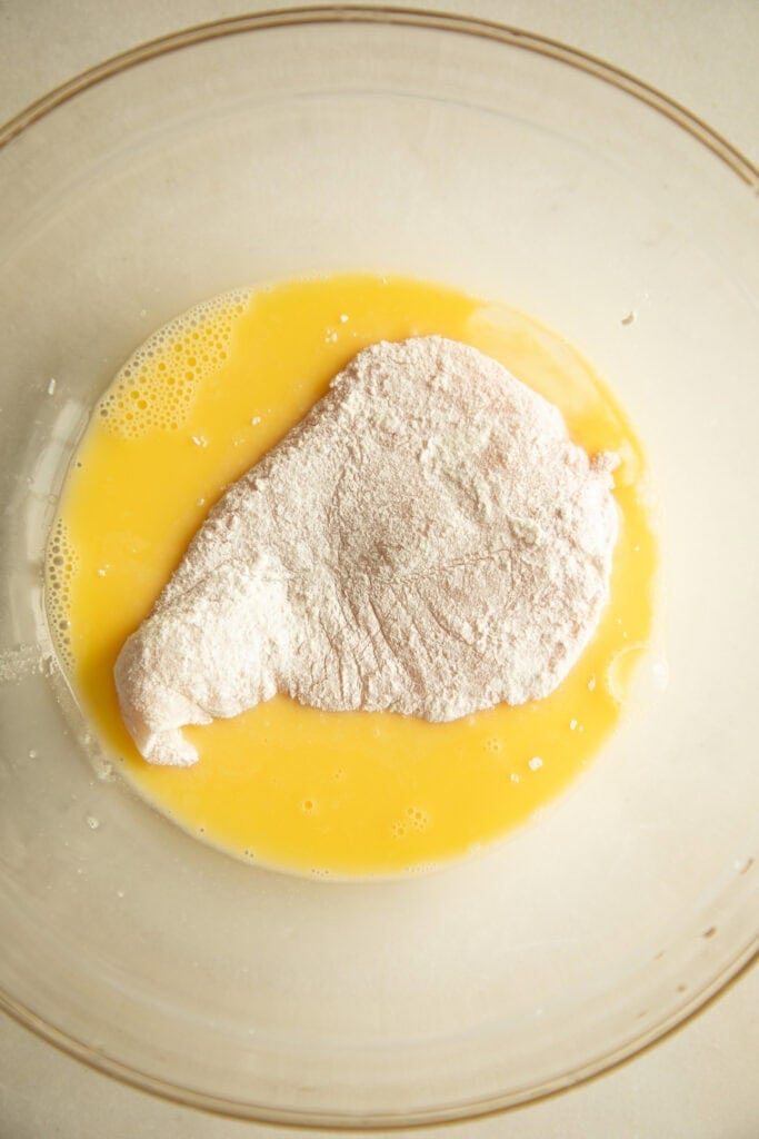 egg mixture in a mixing bowl with a dredged chicken breast